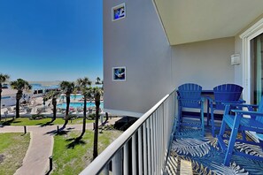 A balcony with a view of a pool and palm trees, a patterned carpet, and a railing.