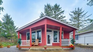 Een rode, gelijkvloerse woning met een veranda, een voordeur en een klein terras.