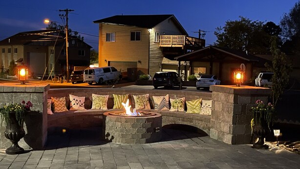 A patio area with a fire pit, stone seating, and a view of a residential neighborhood at dusk. - Cozy Flagstaff Home w/ Outdoor Fire Place (Flagstaff)