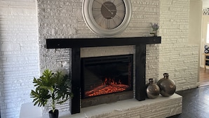 A fireplace with a clock above it, a potted plant, and two decorative vases. - Cozy Flagstaff Home w/ Outdoor Fire Place (Flagstaff)