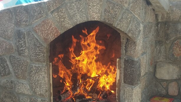 Un horno de pizza exterior de piedra con fuego encendido en su interior.