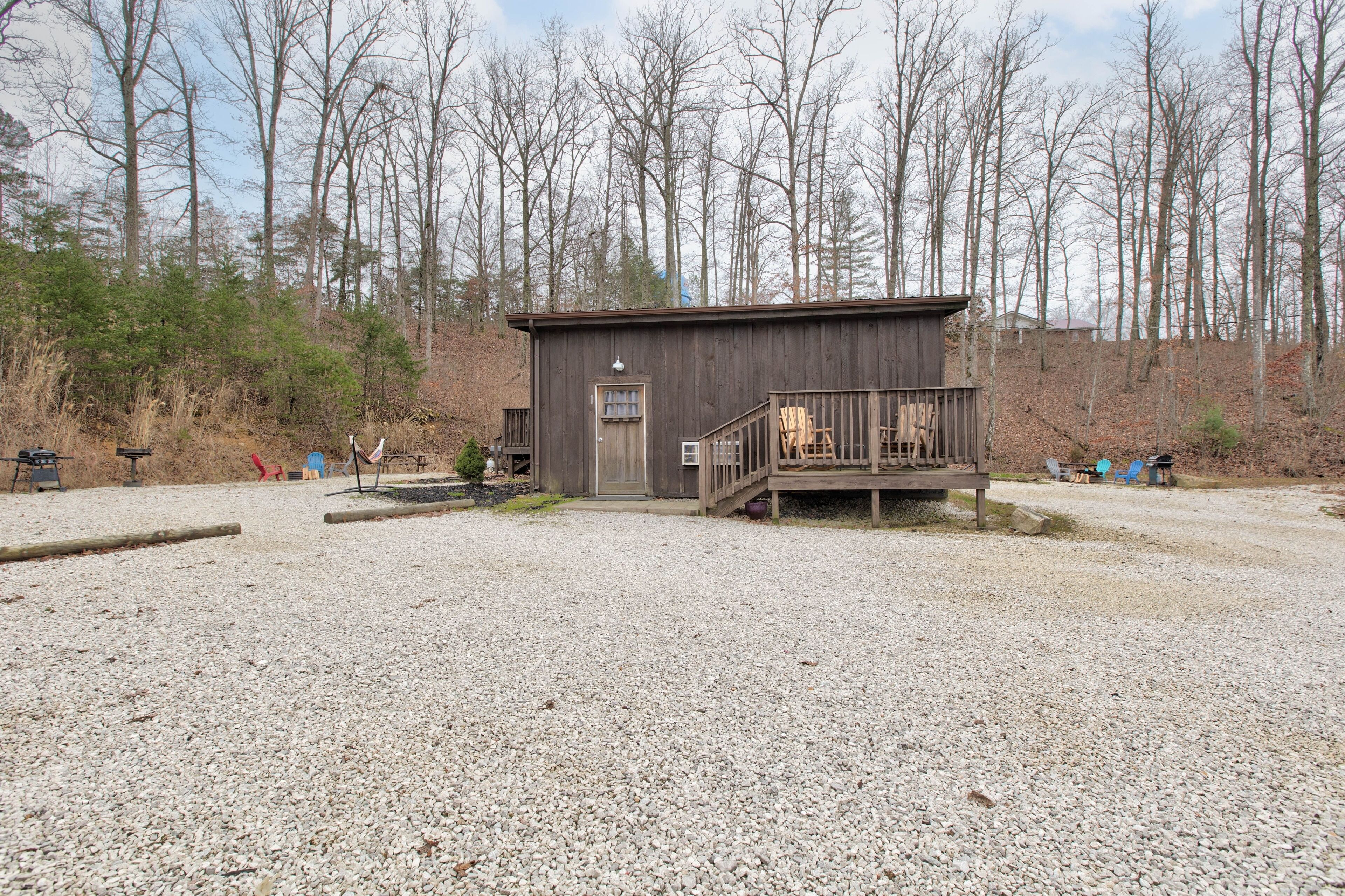 A small wooden cabin with a porch, surrounded by gravel and trees.
