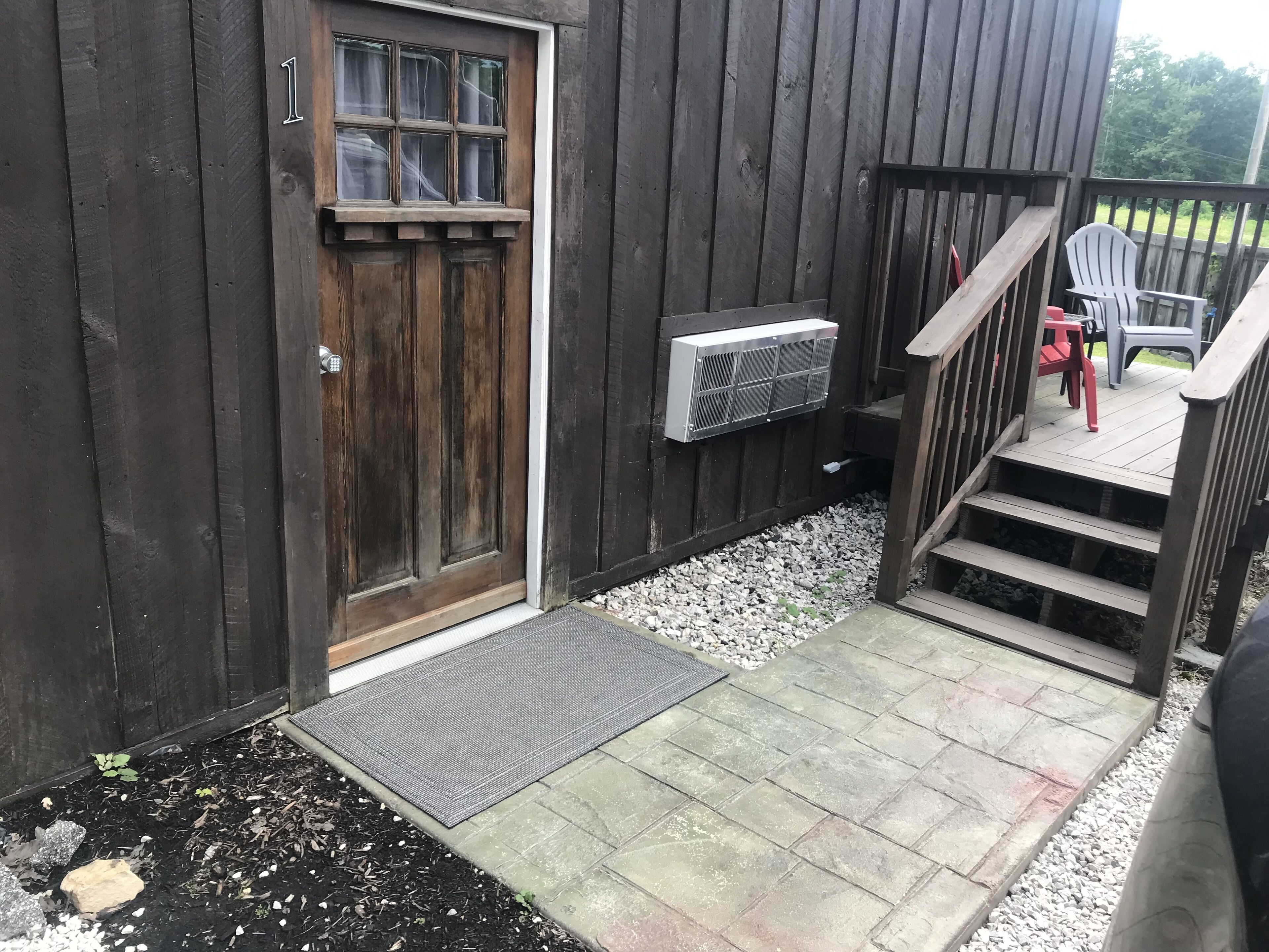 Een houten gebouw met een deur, een klein portaaltje met trappen en buitenmeubilair.