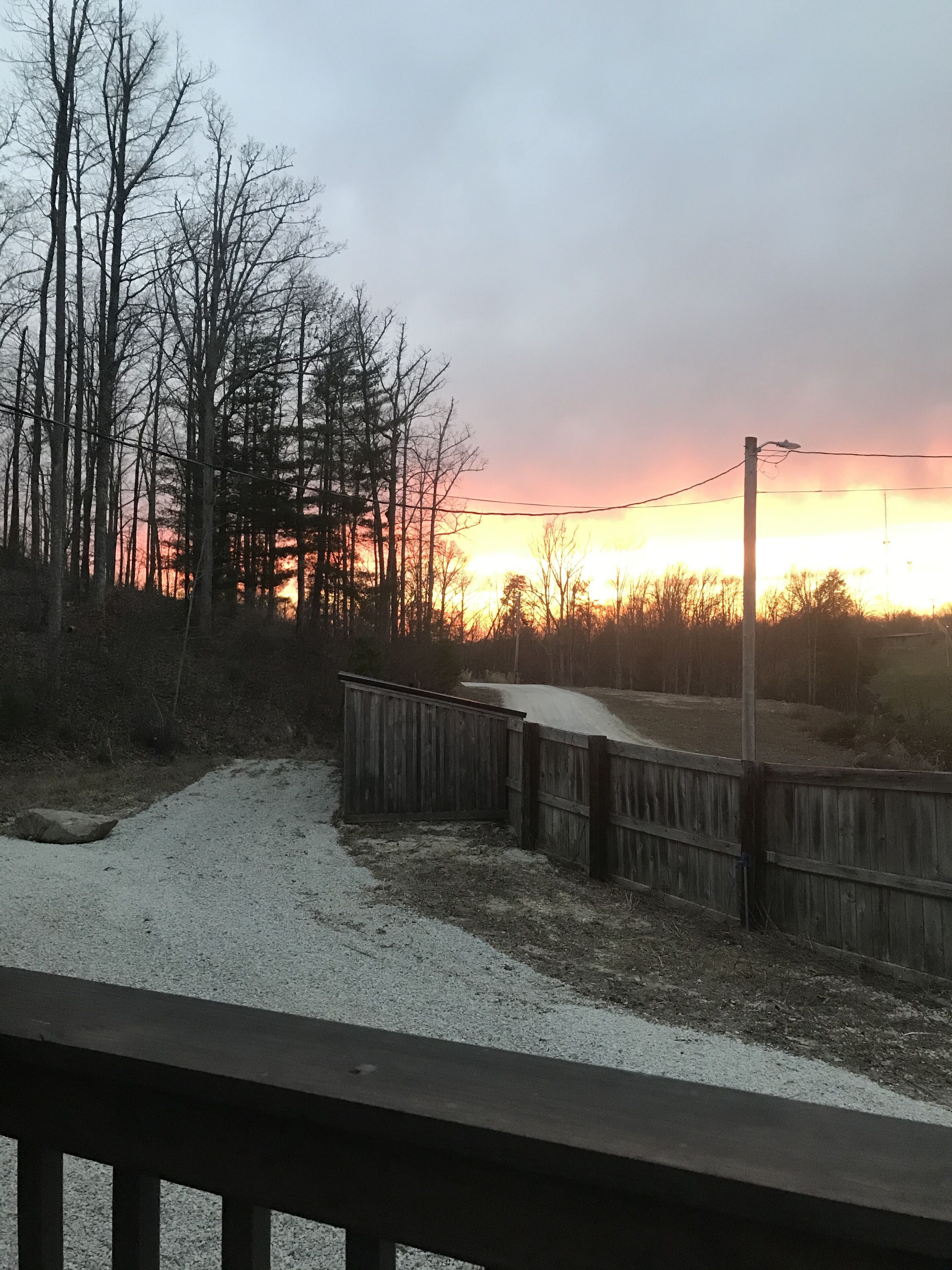 Een grindpad dat leidt naar een houten hek met uitzicht op een bos bij zonsondergang.