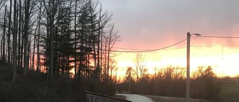 A gravel path leading to a wooden fence with a view of a sunset over a forest.