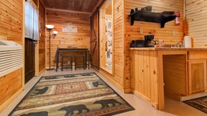 A wooden cabin interior with a kitchen area, a dining table, and a rug with animal patterns. -  TURNING LEAF•Cozy Cabin in the RRG• Couples Retreat (Pine Ridge)