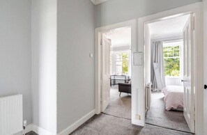 A room with a bed, a desk, and a chair. There are two doors leading to another room.