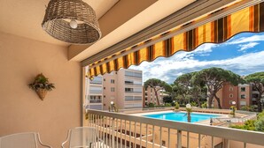 En balkon med udsigt over en pool, hvide møbler og en fletlampe.