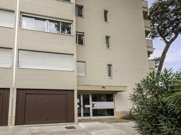A multi-story residential building with a garage door, a small entrance with glass doors, and a tree to the right.