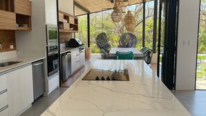 A modern kitchen with a marble island, built-in appliances, and a dining area with rattan chairs. - Eden Roc Villa Luxury 5BR in Hacienda Pinilla (Tamarindo)