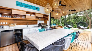 A modern kitchen with a large island, wooden shelves, and a view of greenery outside. - Eden Roc Villa Luxury 5BR in Hacienda Pinilla (Tamarindo)