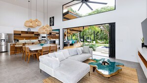 A modern open-plan living area with a large sofa, dining table, and kitchen. - Eden Roc Villa Luxury 5BR in Hacienda Pinilla (Tamarindo)