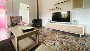Un salon avec un téléviseur, une cheminée, un parquet à motifs et une table en bois.