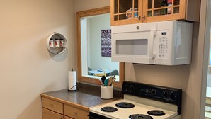 Une cuisine compacte avec des meubles en bois, un four à micro-ondes, une cuisinière et une poubelle.