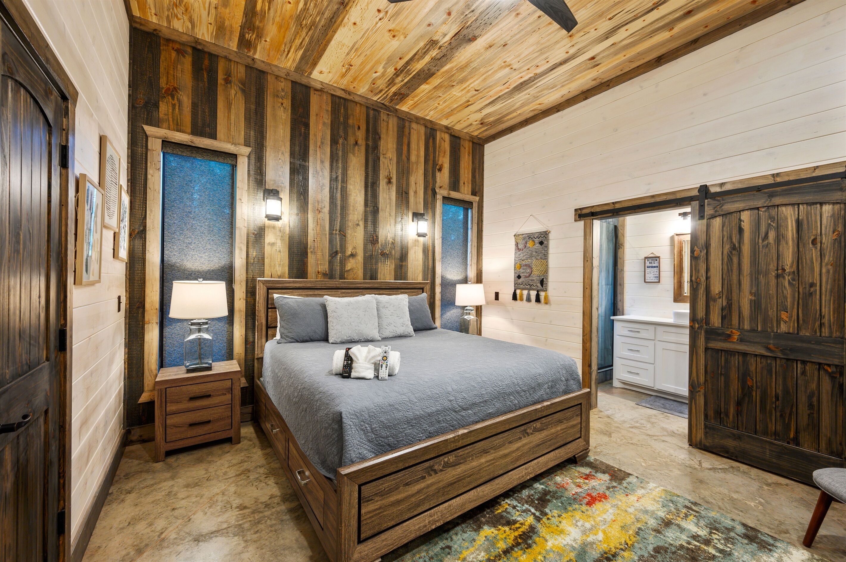 A bedroom with a wooden bed, bedside tables, a nightstand, a large mirror, and a view of the bathroom.