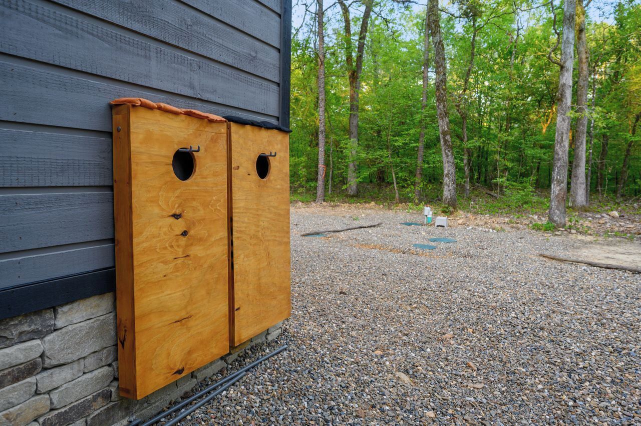 Een houten constructie met twee ronde openingen, naast een gebouw met donkere bekleding en een stenen fundering.