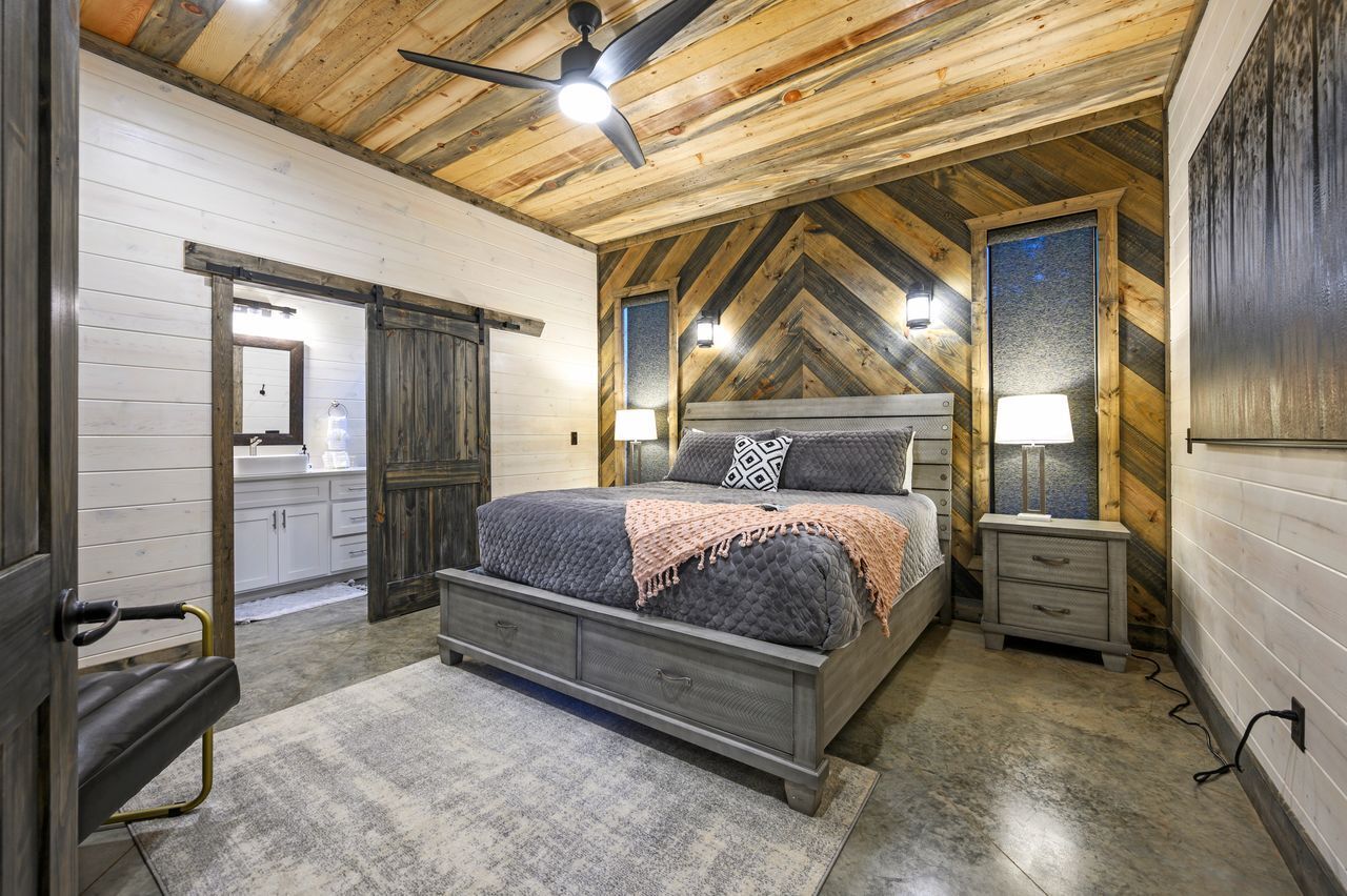 A bedroom with a bed, bedside tables, a ceiling fan, and a wooden ceiling.