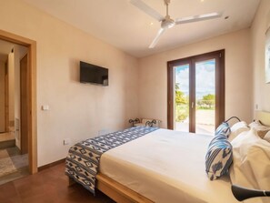 Een slaapkamer met een bed, een plafondventilator, een televisie en een glazen schuifdeur die leidt naar een buitenruimte.