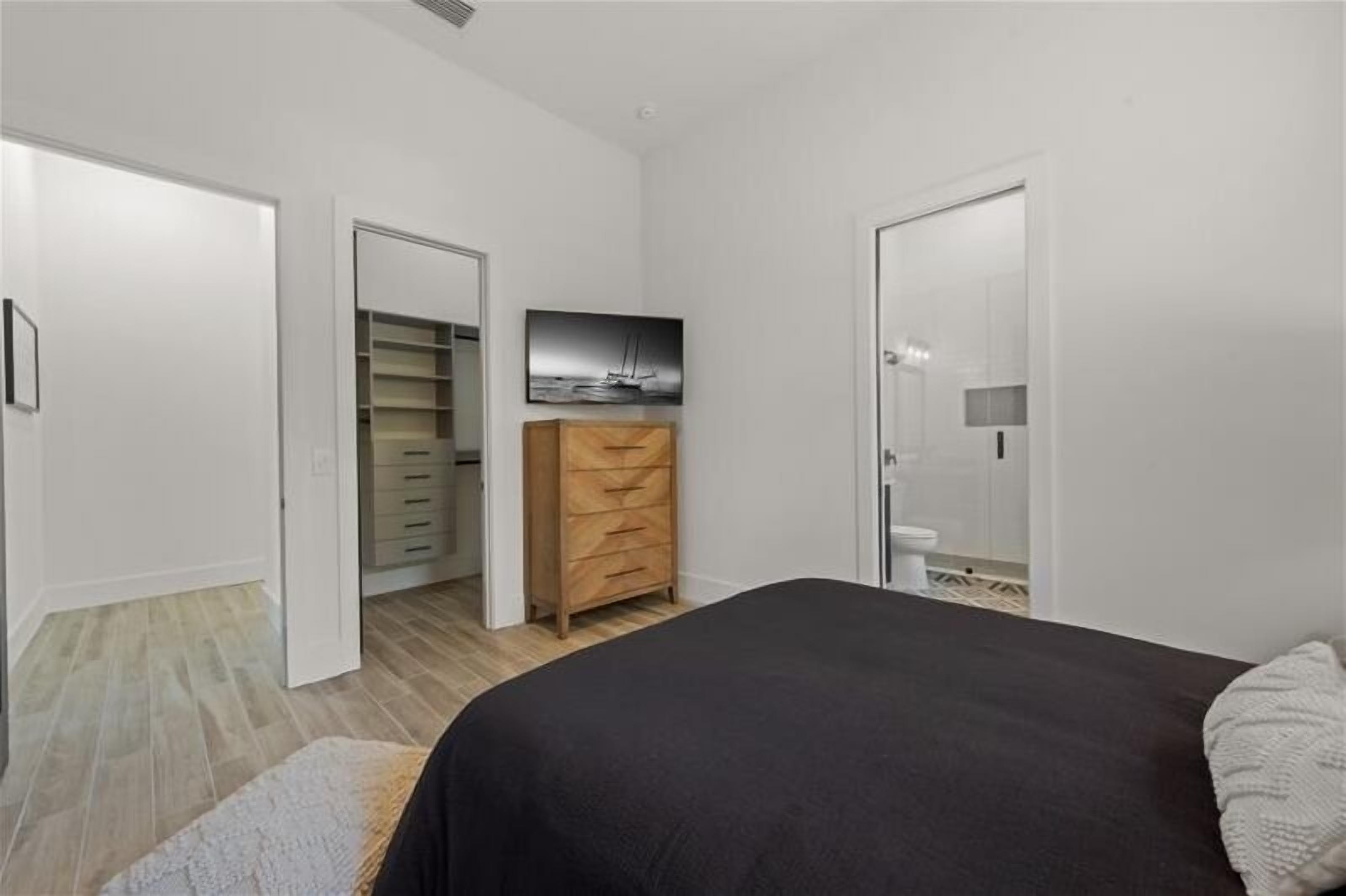 A bedroom with a bed, a wooden dresser, a closet, and a bathroom visible through an open door.
