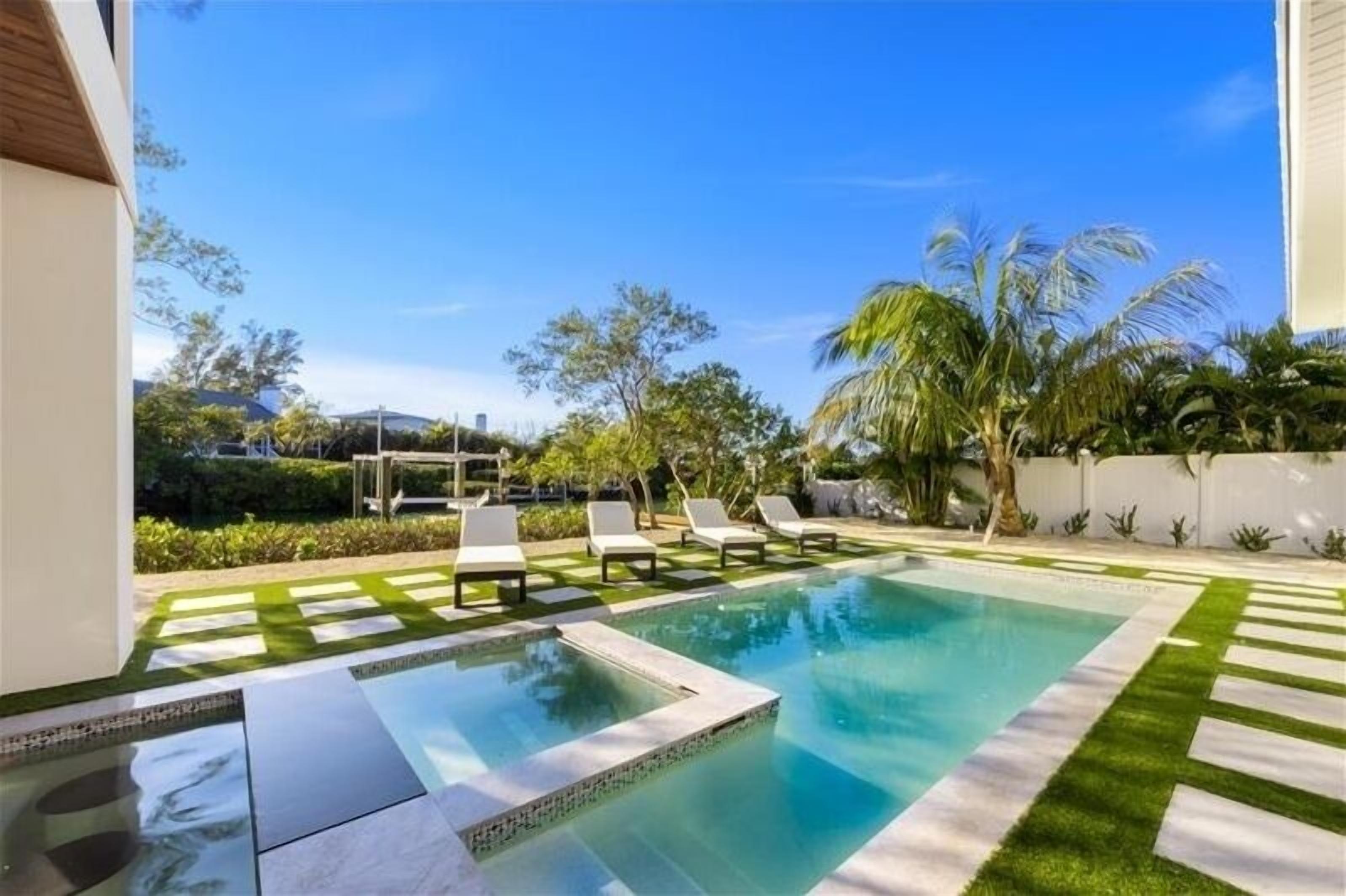 A swimming pool with a tiled deck and lounge chairs, surrounded by greenery and palm trees.