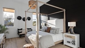 Une chambre à coucher avec un lit à baldaquin, une table de chevet avec une lampe, une chaise et une petite table ornée d’objets décoratifs.