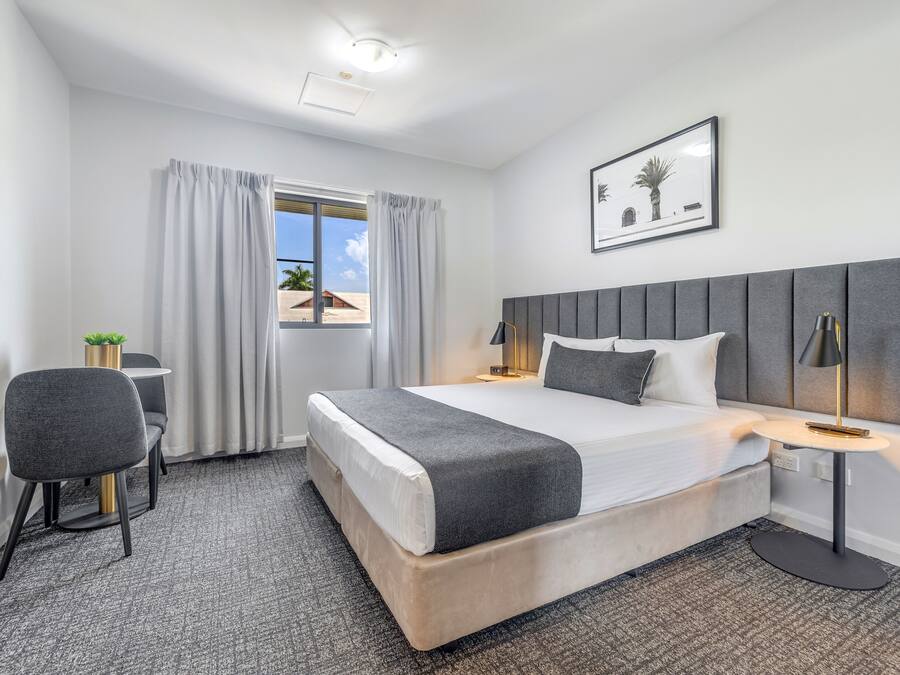 Habitación de hotel con cama, escritorio, silla, ventana con cortinas e imagen enmarcada en la pared.
