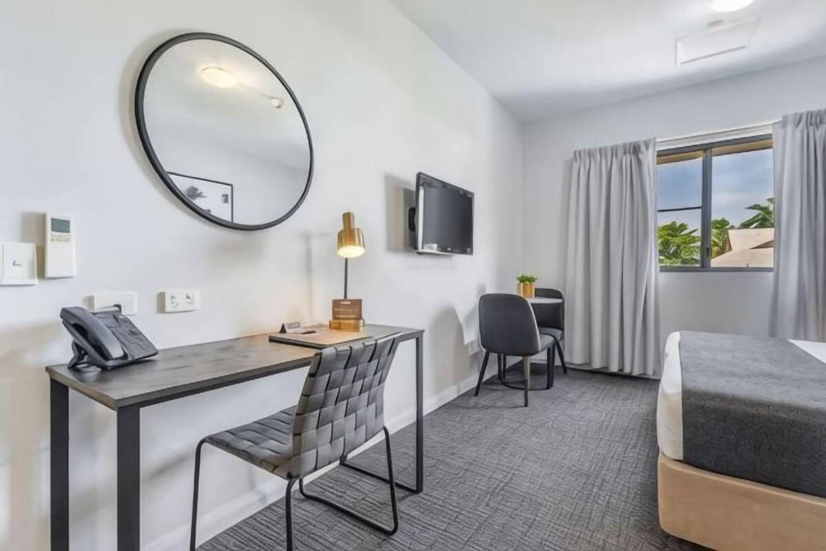 Habitación de hotel con cama, escritorio, silla, televisor y ventana con cortinas.