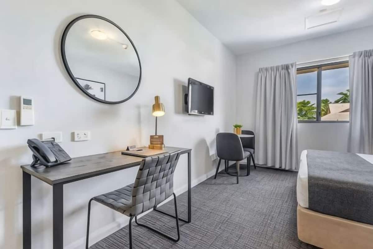 Hotellihuone, jossa on sänky, työpöytä, tuoli, televisio ja ikkuna, jossa on verhot.