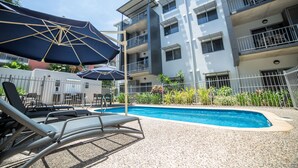 A poolside area with lounge chairs and umbrellas, surrounded by a multi-story building with balconies. - Hudson Parap (Parap)