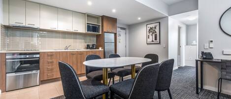 A modern kitchen with a dining area, featuring stainless steel appliances, a microwave, and a refrigerator.