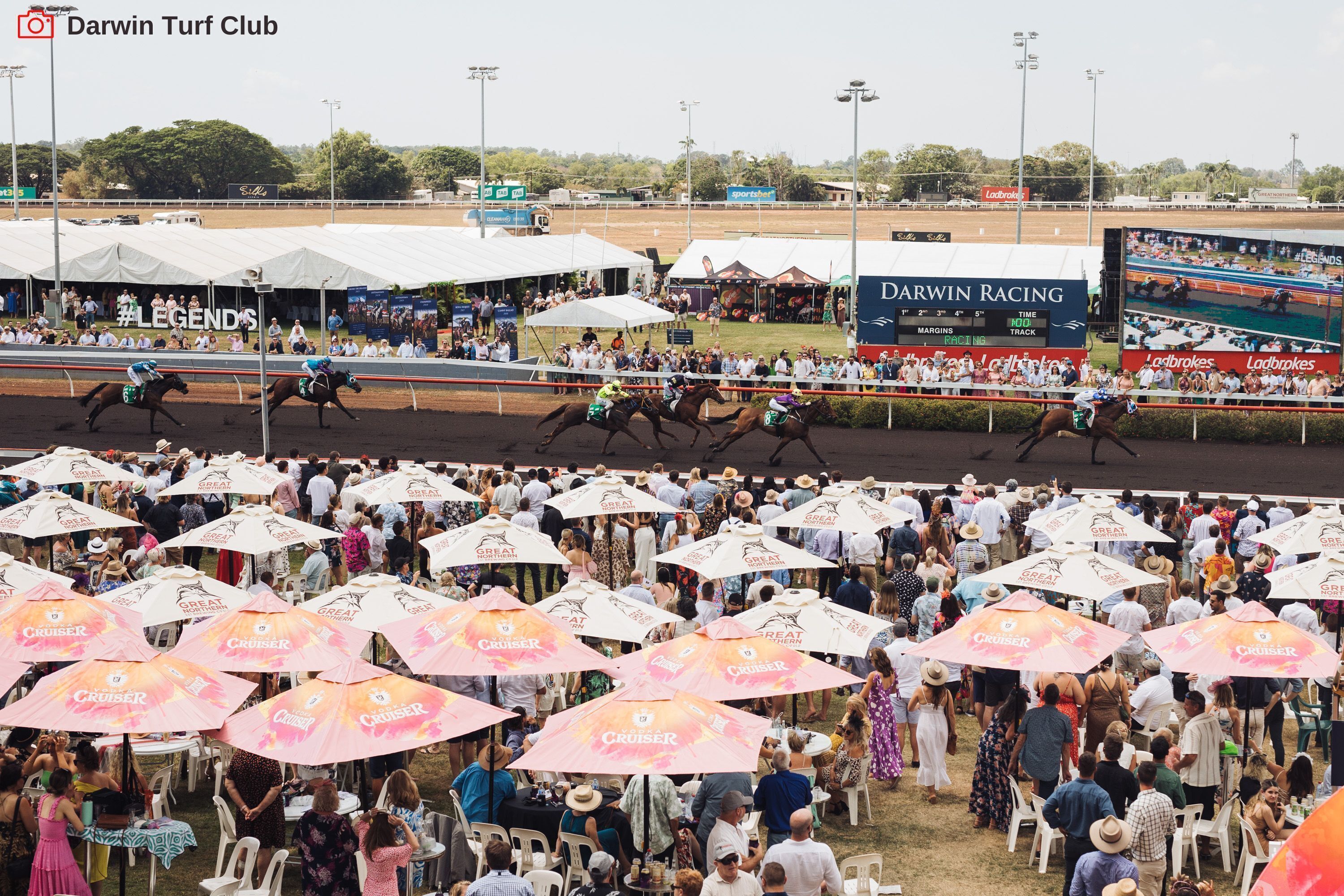 A crowded outdoor event with tents and people under umbrellas.
