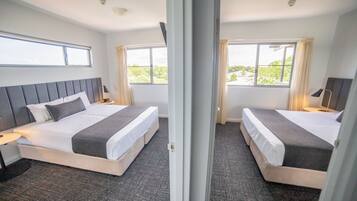 Een hotelkamer met twee bedden, een groot raam en uitzicht op groen.