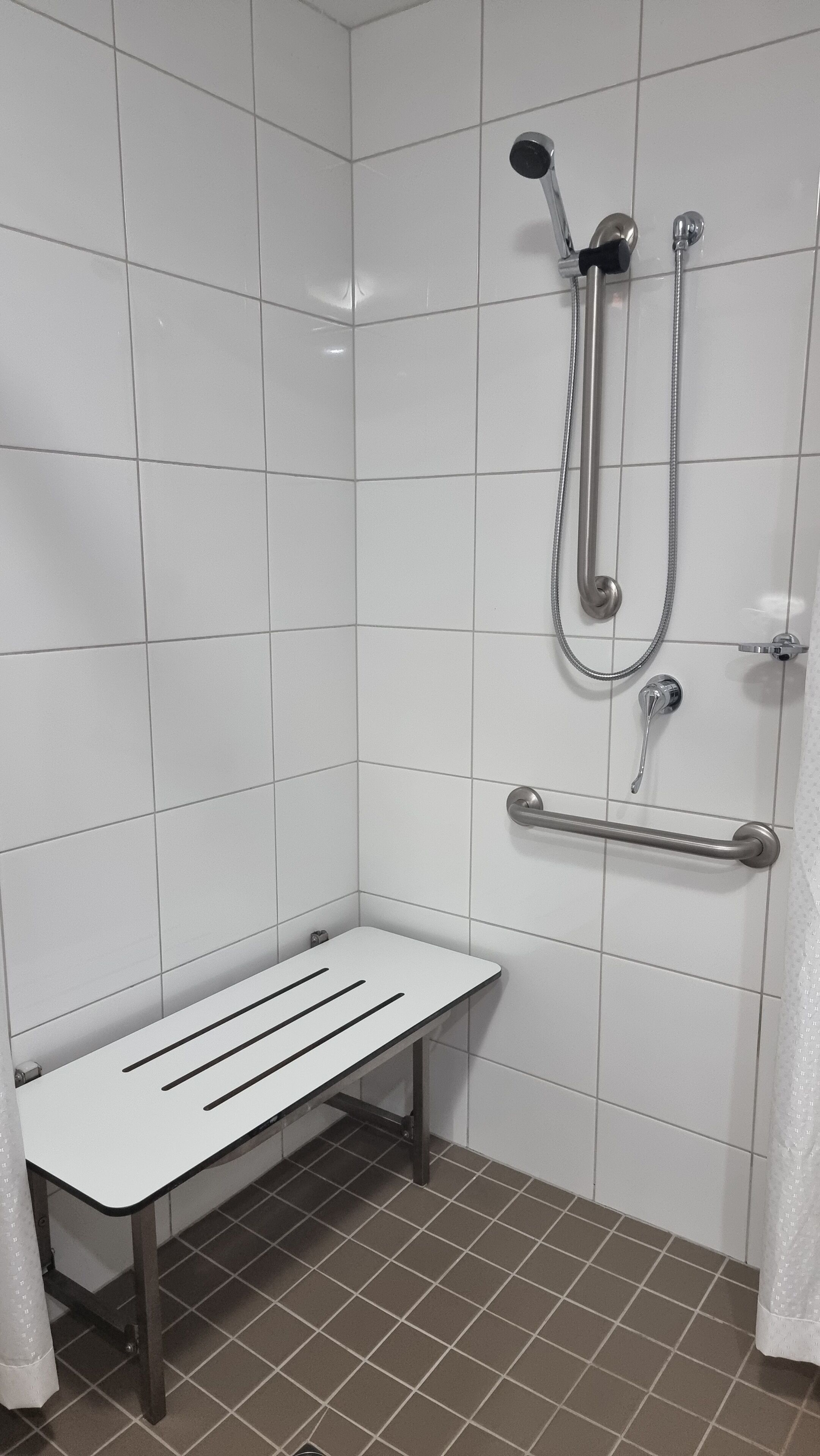 A shower area with a bench, grab bars, and a handheld showerhead.