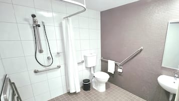 Une salle de bain moderne équipée d’une douche, de toilettes et d’un lavabo, ainsi que de barres d’appui et d’un sèche-mains.