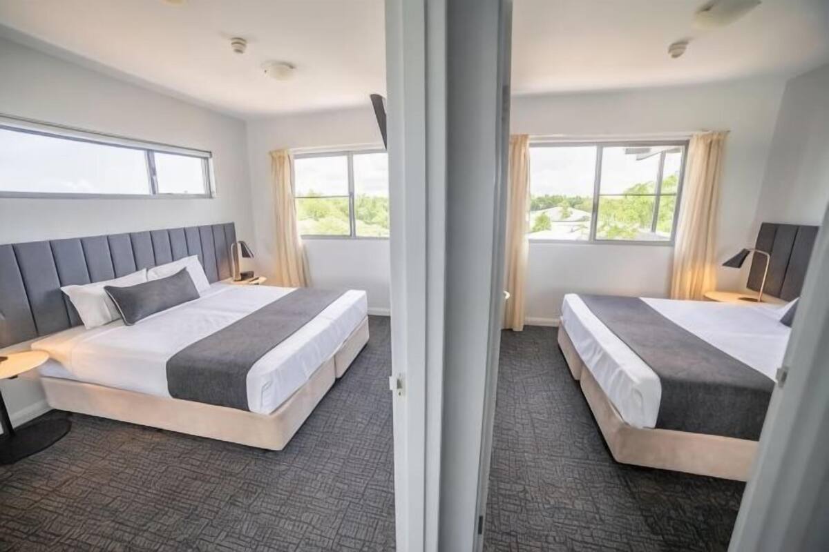 Habitación de hotel con dos camas, un ventanal grande y vistas a zonas verdes.