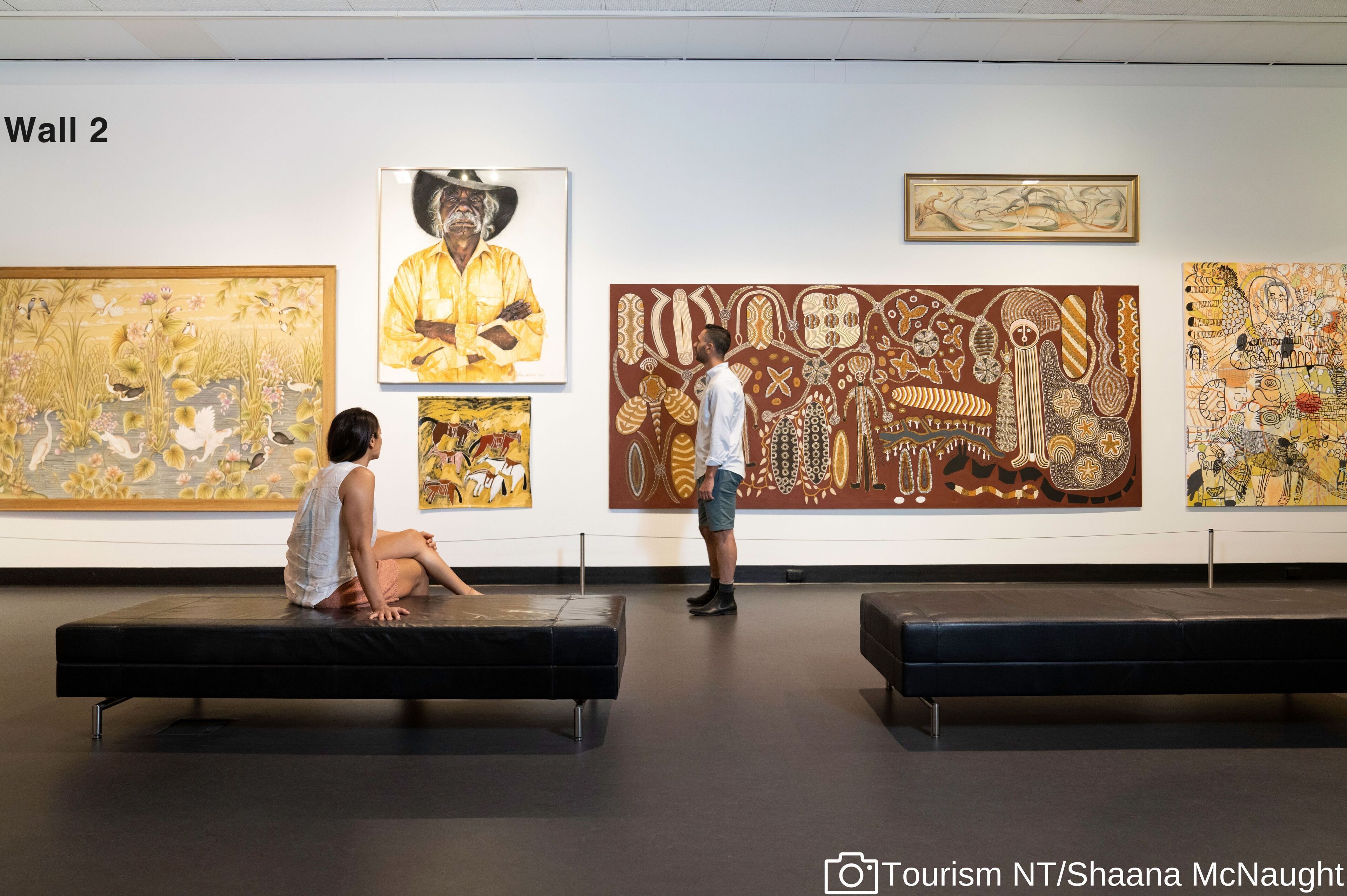 An art gallery with various paintings on display, benches for viewing, and a wall labeled "Wall 2".