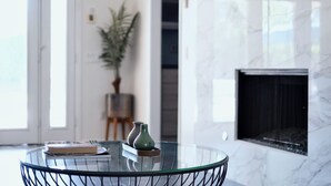 A glass-top table with a book and two vases, a potted plant, and a fireplace in a modern interior. - Relax in Palm Springs Pool, Spa, EV Charger, Views (Palm Springs)
