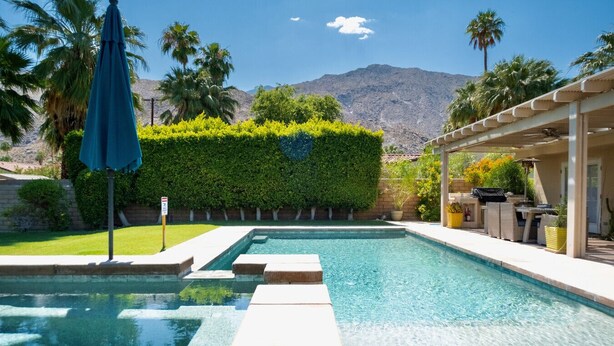 A swimming pool with clear blue water, surrounded by a well-maintained hedge and palm trees. - Relax in Palm Springs Pool, Spa, EV Charger, Views (Palm Springs)