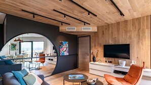 A modern living room with a sofa, coffee table, and orange chair. There is a TV on the wall and a painting on the wall. - Stanatura by Interhome (Porto Vecchio)