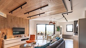 A modern living room with a wooden ceiling, a TV, a sofa, and a dining area with a view. - Stanatura by Interhome (Porto Vecchio)