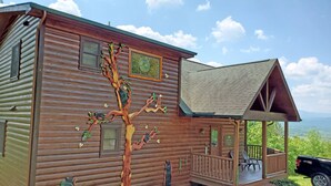 A wooden cabin with a porch, a large tree mural, and a view of the mountains.