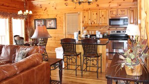 A wooden cabin interior with a dining area, kitchen, and a leather sofa.