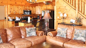 A cozy cabin interior with a leather sofa, wooden dining table, and a kitchen with wooden cabinets and a microwave.