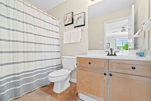 A bathroom with a striped shower curtain, a toilet, a sink with a mirror, and a towel rack. - 3 Min Walk to Beach!  4BR + Bikes + Paddleboard! (Miramar Beach)
