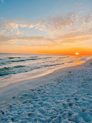 Een strand met golven en een ondergaande zon.