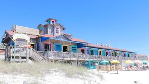 A beachside building with multiple colorful rooms, a wooden staircase, and outdoor seating areas.