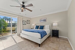 A bedroom with a bed, a ceiling fan, a nightstand, and a view of the outdoors. - 3 Min Walk to Beach!  4BR + Bikes + Paddleboard! (Miramar Beach)