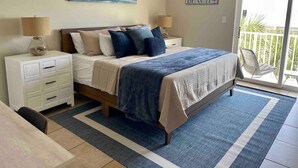 A bedroom with a bed, nightstands, a lamp, a painting, and a balcony with a view.