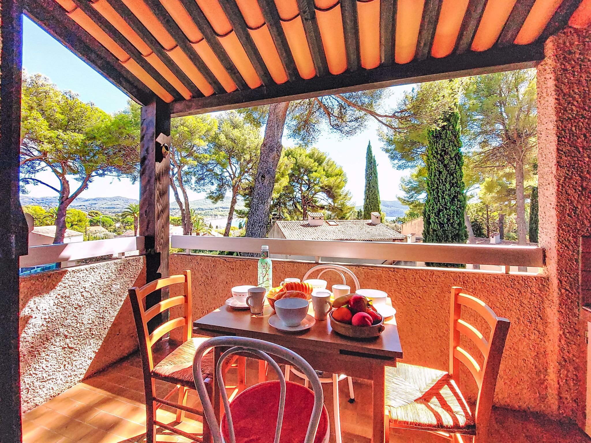 A terrace with a table set for two, chairs, and a view of trees and hills.