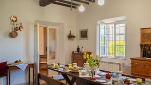 A dining area with a wooden table set for a meal, a window with a view of greenery, and a kitchen area with copper cookware hanging on the wall. - Wonderful private villa with A/C, private pool, WIFI, TV and panoramic view, close to San Gimign... (Gambassi Terme)